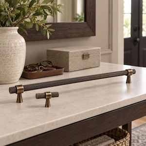 May include: A long dark bronze cabinet pull and a matching smaller cabinet knob. Both pieces feature a textured, knurled cylindrical bar design with smooth, conical-shaped mounting posts in a polished brass finish at each end.