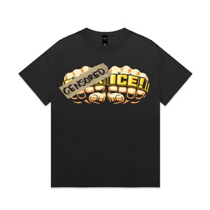 Puede incluir: Una camiseta negra de manga corta con un gráfico de dos puños cerrados con puños americanos dorados. Una cinta de color canela cubre el puño izquierdo con la palabra CENSORED, mientras que el puño derecho muestra la palabra ICE!.