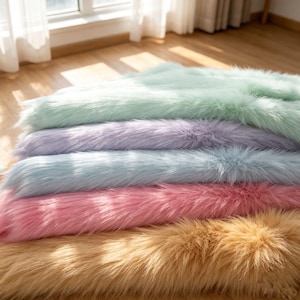 Könnte beinhalten: Ein Stapel aus fünf rechteckigen Kunstfelldecken in Pastellfarben. Die oberste Schicht ist mintgrün, gefolgt von Lavendel, Hellblau, leuchtendem Pink und einer goldbraunen Basisschicht. Jede Decke hat eine lange, weiche und zottelige Textur.