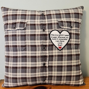 Könnte beinhalten: Ein graues und weißes kariertes Kissen mit einem herzförmigen Patch, auf dem steht "This is a shirt I used to wear. Whenever you hold it remember I am there. Love, Karl".