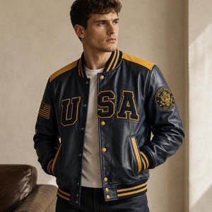 May include: A navy blue varsity jacket with yellow accents, featuring the letters USA in large yellow lettering on the chest, a United States flag patch on the right sleeve, and a circular United States emblem patch on the left sleeve.