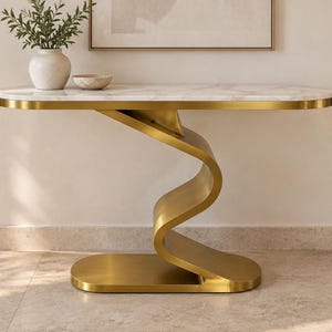 May include: A console table featuring a white marble top with grey veining and a gold-finished metal base. The base consists of a single, continuous, S-shaped curved support connecting the rectangular top to a flat, oval-shaped floor base.