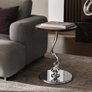 May include: A side table with a circular dark wood top and a reflective silver-toned metal base. The base features a central vertical support with a twisted, ribbon-like design that connects to a flat, circular, polished silver-toned metal floor plate.