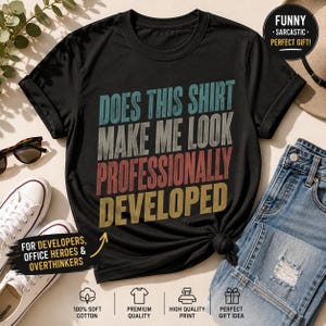 May include: A black short-sleeved t-shirt featuring the text "DOES THIS SHIRT MAKE ME LOOK PROFESSIONALLY DEVELOPED" in stacked lines of teal, grey, red, and yellow. The shirt has a crew neckline and a casual fit, displayed with denim jeans.
