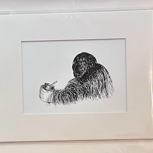 May include: A black and white pen and ink drawing of an orangutan holding a small cup with a spoon. The artwork is framed in a white mat and encased in a clear plastic sleeve.