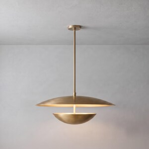 May include: A brass pendant light fixture featuring a large, shallow, disc-shaped upper shade and a smaller, bowl-shaped lower shade. The two components are connected by a central vertical rod that extends upward to the ceiling mount.