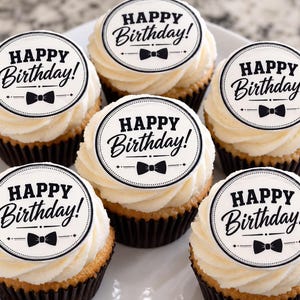 May include: Six cupcakes with white frosting, each topped with a circular white edible topper featuring the black text Happy Birthday! and a black bow tie graphic. The cupcakes are in dark brown paper liners and arranged on a white plate.