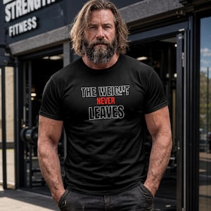 Könnte beinhalten: Ein schwarzes Kurzarm-T-Shirt mit dem weiß umrandeten Text THE WEIGHT und LEAVES sowie dem Wort NEVER in roter Schrift in der Mitte. Das T-Shirt hat einen Rundhalsausschnitt und besteht aus einem einfarbigen schwarzen Stoff.