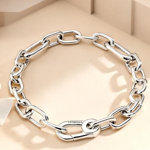 May include: A silver-toned chain link bracelet featuring elongated, polished oval links connected in a continuous loop. The bracelet includes a prominent, larger oval-shaped clasp mechanism with a spring-loaded gate, providing a secure closure.