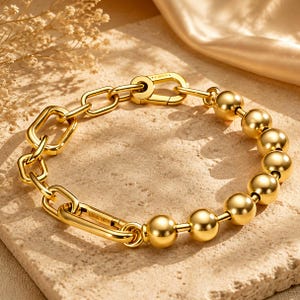 May include: A gold-toned bracelet featuring a combination of polished spherical beads and rectangular chain links. The design includes a secure lobster-style clasp mechanism, creating a mixed-texture aesthetic with a high-shine metallic finish.