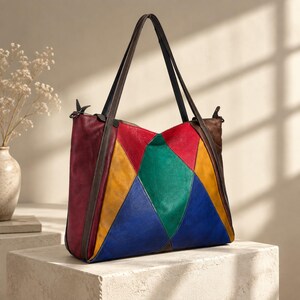 Puede incluir: Un bolso tote de cuero multicolor con un diseño geométrico de patchwork en tonos rojo, amarillo, verde y azul. El bolso incluye paneles laterales de cuero marrón oscuro, dos correas de hombro a juego y un cierre de cremallera superior.