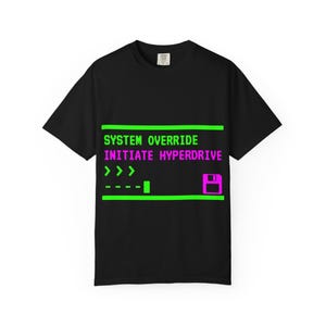 May include: A black short-sleeve t-shirt featuring a graphic print with neon green and pink text that reads SYSTEM OVERRIDE INITIATE HYPERDRIVE, accompanied by a progress bar, arrow symbols, and a floppy disk icon centered on the chest area.