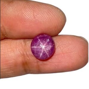 Può includere: Una gemma di rubino stellato a taglio cabochon rotondo, caratterizzata da un colore magenta-rosa intenso e da un distinto motivo a stella bianca a sei punte che appare sulla superficie della pietra quando la luce riflette.