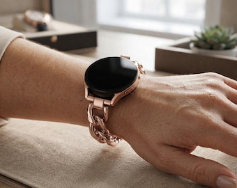 Może przedstawiać: Smartwatch z okrągłym czarnym wyświetlaczem i metalową bransoletą z ogniw w kolorze różowego złota. Zegarek posiada polerowane wykończenie koperty oraz zazębiające się ogniwa bransolety, tworząc spójny wygląd na nadgarstku.