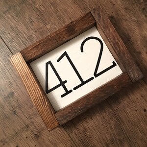 May include: A wooden framed sign with the number 412 painted in black on a white background.