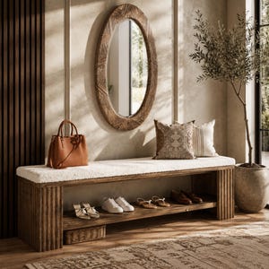 May include: A wooden entryway bench with a white textured cushion, featuring a lower shelf holding various shoes and a woven basket. Above the bench hangs an oval mirror with a carved wooden frame, a brown leather handbag, and two decorative pillows.
