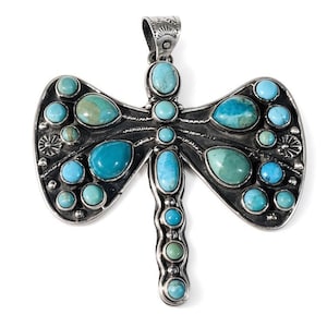 May include: A dragonfly-shaped pendant crafted from oxidised silver, featuring multiple inlaid turquoise stones in various shades of blue and green. The wings and body are adorned with round and teardrop-shaped cabochons, with a decorative bail at the top.