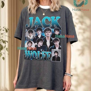 Puede incluir: Una camiseta gris carbón de manga corta con un estampado gráfico de Jack Wolfe. El diseño incluye el texto JACK WOLFE en una fuente con degradado azul, rodeado de varios retratos fotográficos sobre un fondo de relámpagos azules.