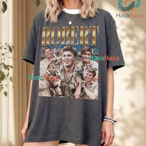 May include: A charcoal gray short-sleeve t-shirt featuring a graphic print with the name ROBERT in gold lettering above a collage of photographs showing individuals interacting with koalas. The shirt has a crew neckline and a relaxed fit.