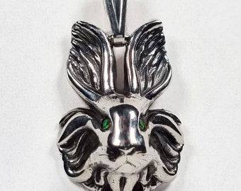 May include: A silver pendant in the shape of a rabbit with green gemstone eyes. The rabbit has large, detailed ears and a fluffy body.