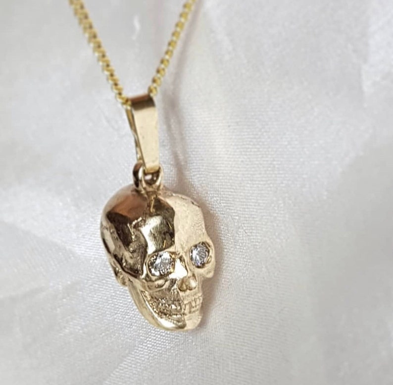 May include: A gold skull pendant necklace with two clear diamond-like stones for eyes.