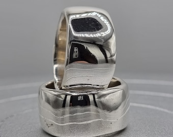 May include: Two silver rings stacked on top of each other. The top ring has a smooth, rounded surface, while the bottom ring has a textured, hammered surface.