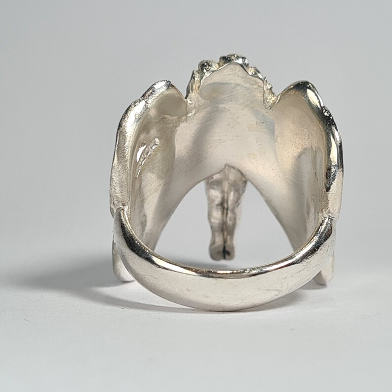 May include: Silver ring with a unique, abstract design. The ring is open in the back and has a textured, organic shape.