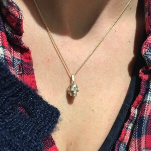 May include: A gold chain necklace with a small, detailed skull pendant. The skull has small, clear stones for eyes.