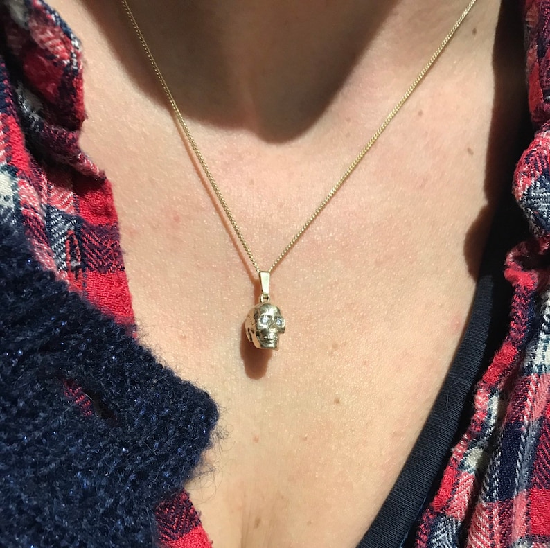 May include: A gold chain necklace with a small, detailed skull pendant. The skull has small, clear stones for eyes.