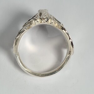 May include: A silver ring with a detailed design, featuring a raised, textured, organic shape.