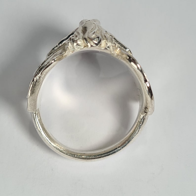 May include: A silver ring with a detailed design, featuring a raised, textured, organic shape.