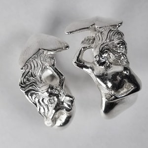 May include: Two silver rings with detailed sculptures of a woman holding a mushroom. The rings are made of polished silver and have a smooth, shiny finish.