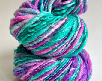 May include: A skein of yarn in shades of teal, purple, and pink. The yarn is hand-dyed and has a variegated color pattern.