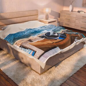 Puede incluir: Una manta de felpa con un estampado vibrante de alta resolución de una escena costera con olas del océano de color azul profundo rompiendo contra un muelle de madera y una playa de arena, colocada sobre una cama con cabecero neutro.