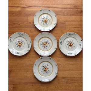 May include: Five round ceramic plates with scalloped edges, each featuring a central floral motif of yellow, red, and blue flowers surrounded by a thin yellow circular band and small green leaf accents along the outer rim.