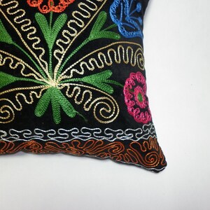 May include: Black velvet pillow with colorful embroidered floral design. The pillow features a central floral motif with green leaves, gold swirls, and pink, blue, and orange flowers.