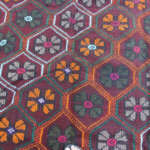 May include: A close-up of a red, green, and orange patterned rug with a geometric design. The rug has a repeating pattern of flowers.