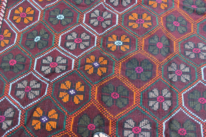 May include: A close-up of a red, green, and orange patterned rug with a geometric design. The rug has a repeating pattern of flowers.