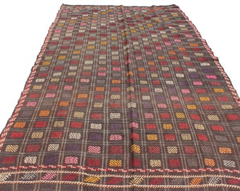 May include: A vintage Turkish rug with a geometric pattern in shades of brown, red, pink, and white. The rug has a woven border with a repeating design.