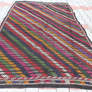 May include: A colorful handwoven rug with a geometric pattern in shades of red, green, yellow, purple, and white on a black background.