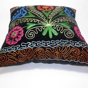 May include: Black velvet pillow with colorful embroidered floral designs. The pillow has a border of orange, white, and silver embroidery.
