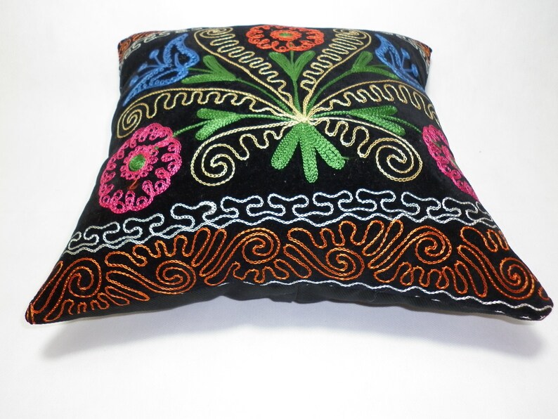 May include: Black velvet pillow with colorful embroidered floral designs. The pillow has a border of orange, white, and silver embroidery.