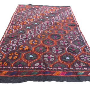 May include: A traditional Turkish rug with a geometric pattern of red, orange, green, and blue flowers on a dark brown background. The rug has a black border with a multi-colored stripe.