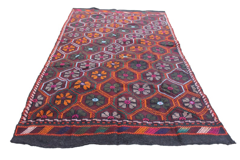 May include: A traditional Turkish rug with a geometric pattern of red, orange, green, and blue flowers on a dark brown background. The rug has a black border with a multi-colored stripe.