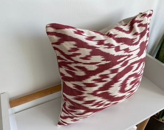 May include: A red and white patterned throw pillow with an ikat design. The pillow is made of a soft, woven fabric and has a zipper closure.