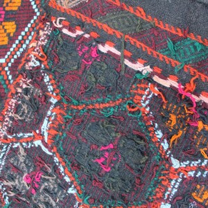 May include: Close-up of a colorful woven rug with a geometric pattern. The rug is made of wool and has a frayed edge. The colors are red, orange, green, blue, and white.