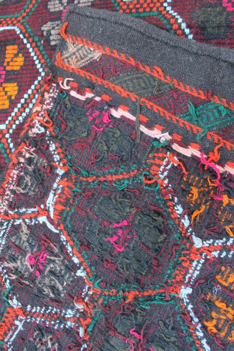May include: Close-up of a colorful woven rug with a geometric pattern. The rug is made of wool and has a frayed edge. The colors are red, orange, green, blue, and white.