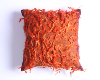 May include: Orange and brown throw pillow with a textured, fuzzy surface. The pillow has a decorative design with a fringe border.