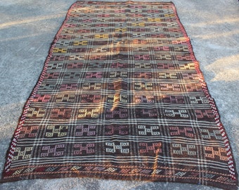 May include: A brown, beige, and pink woven rug with a geometric pattern. The rug has a fringe border.