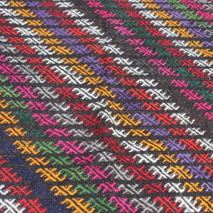 May include: A close-up of a colorful woven rug with a geometric pattern. The rug is made of wool and has a variety of colors, including red, green, blue, yellow, and white.